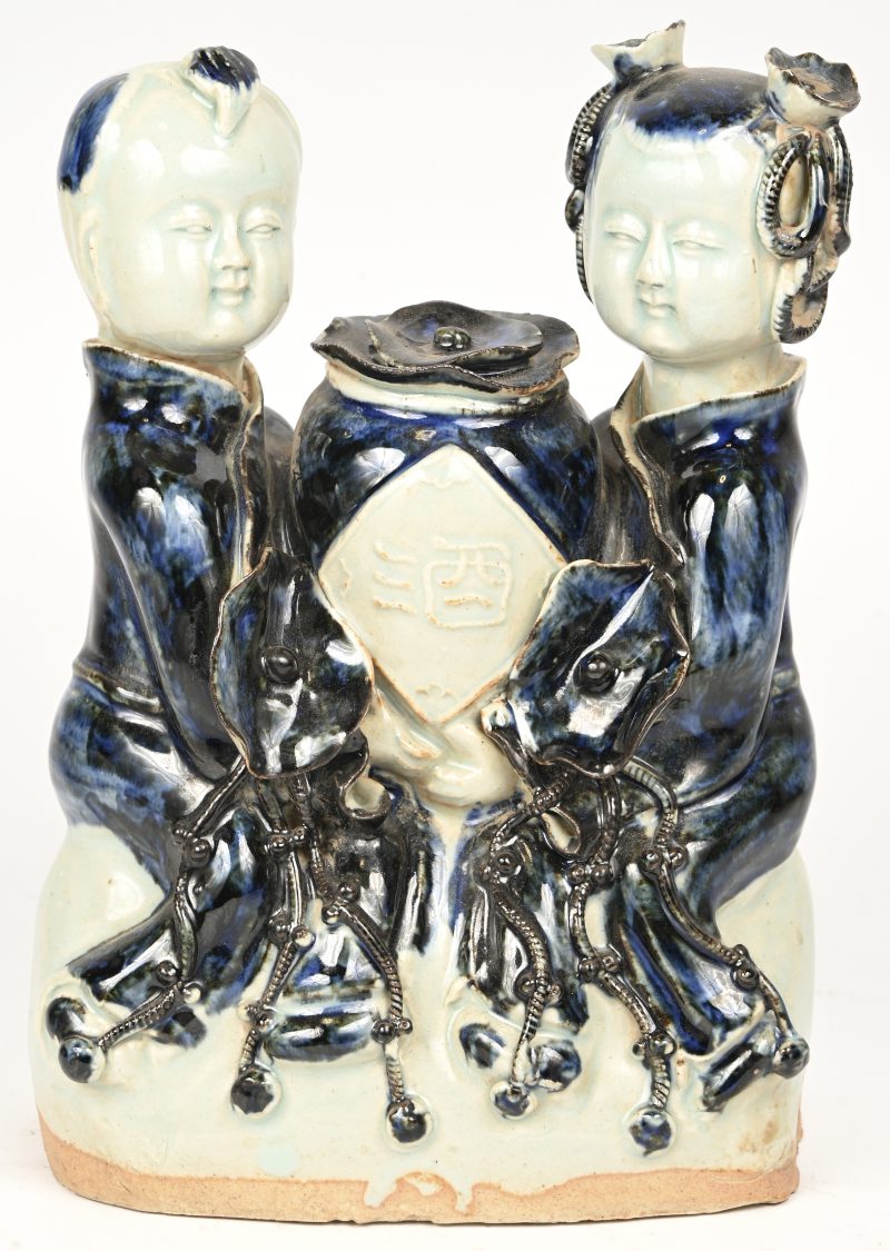Een dekselvaasje geflankeerd door twee kinderen van blauw en wit porselein. Chinees werk.