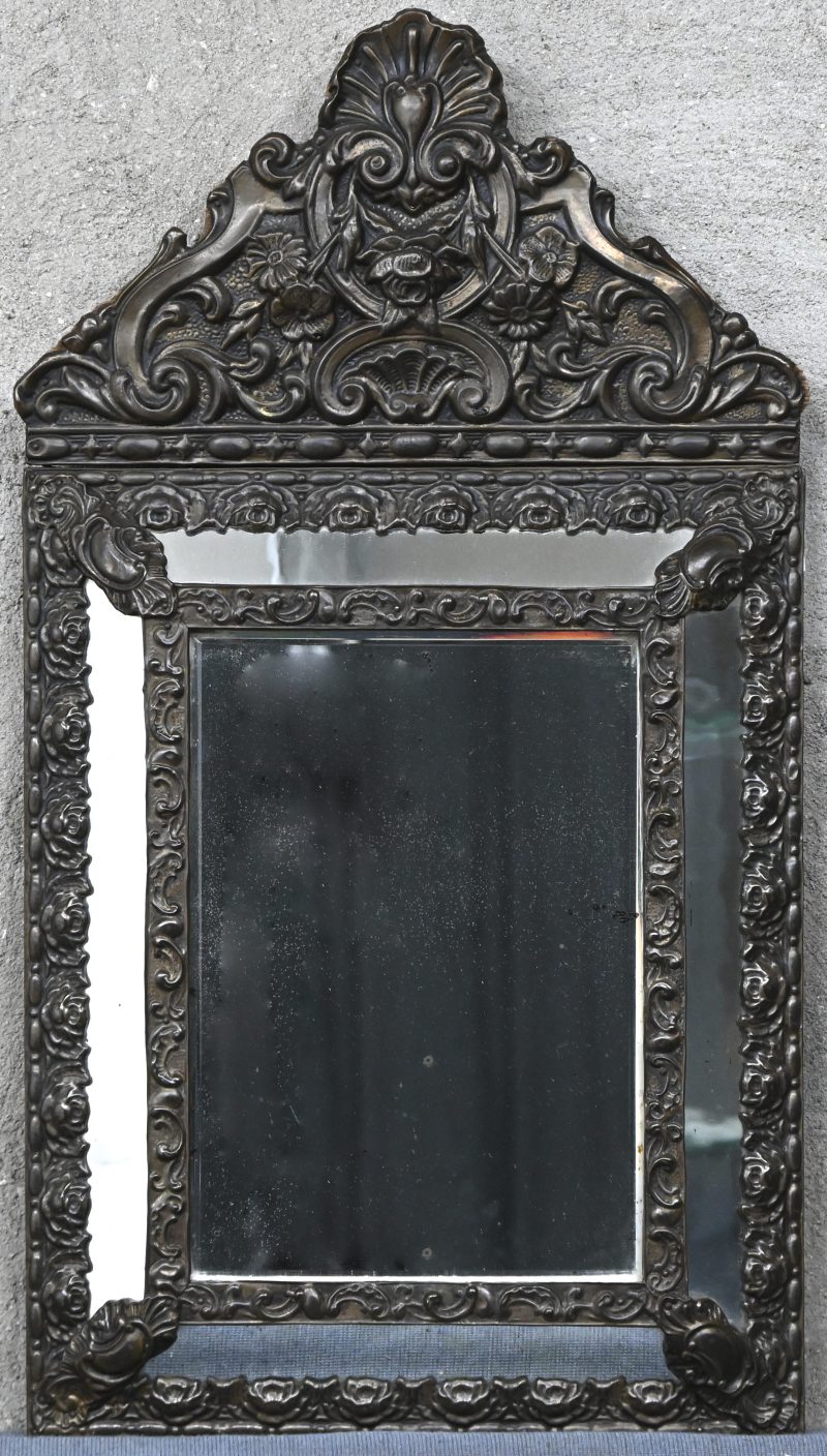 Een barokke spiegel met een gedreven koperen lijst met floraal motief.