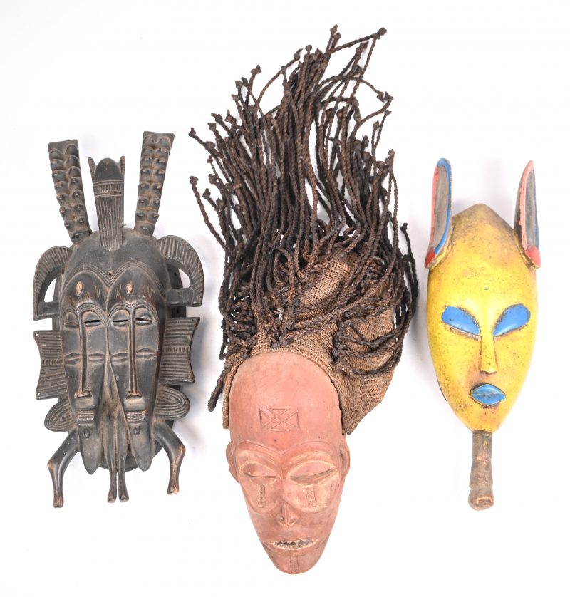Een lot van drie Afrikaanse maskers in hout waarvan één geel, één zwart en één rood met dreads.