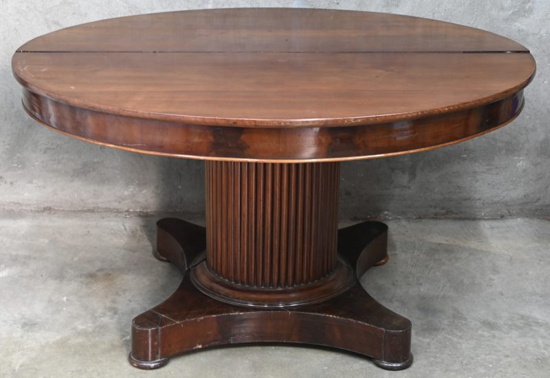 Een verlengbare ovalen tafel in acajou op een centrale zuilvormige poot, uitschuifbaar met extra centrale poot. Verlengbaar met 2 x 42.5 cm.