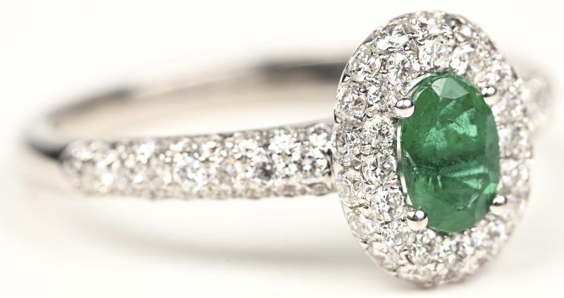 Een 18 kt witgouden ring bezet met centrale smaragd van +- 0,40 ct. En briljanten met een gezamenlijk gewicht van +- 0,75 ct.