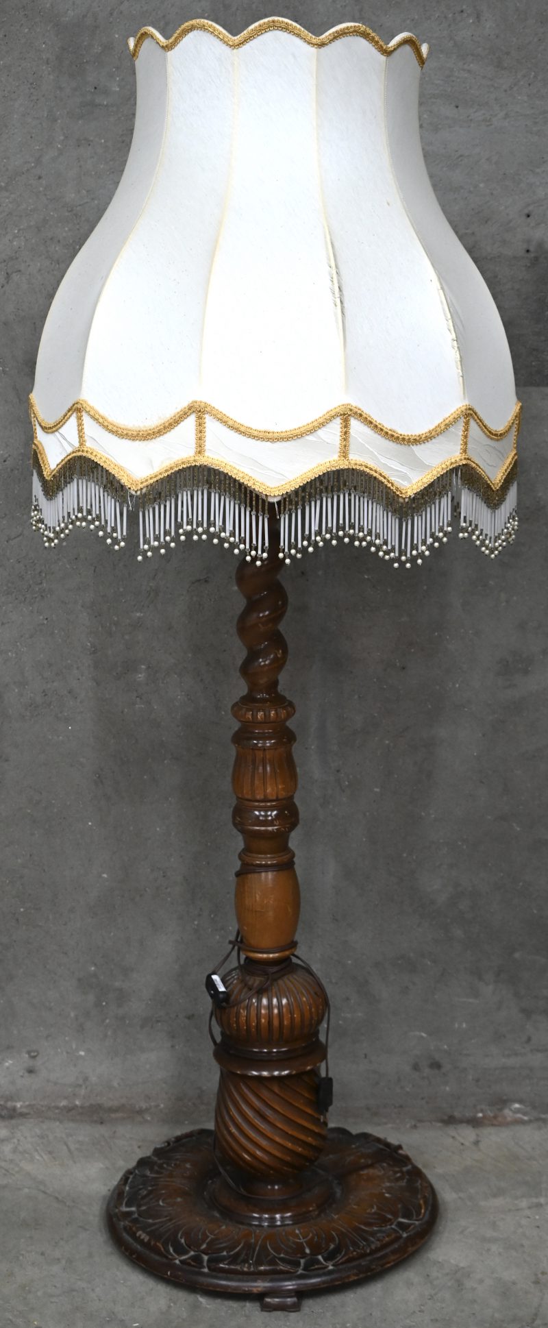Een een hout gesculpteerde staande lamp met gedraaide arm en grote kap.