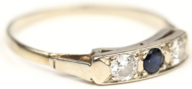 Een 14 kt witgouden ring bezet met twee diamanten en één saffier met een gezamenlijk gewicht van +- 0,30 ct.