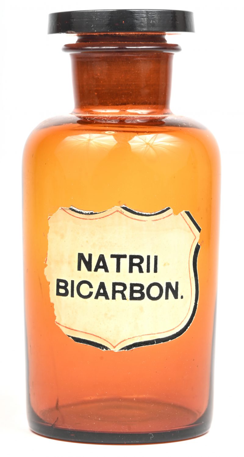 Een amberkleurig, glazen apotheker pot. Label met opschrift “NATRII BICARBON.”.