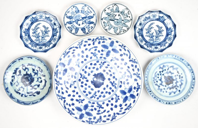 Een lot van 7 Chinees blauw-wit porseleinen schoteltjes en bijgevoegd bord. Verschillende merktekens onderaan, waaronder Qing en Kangxi, 17e tot 19e eeuw.