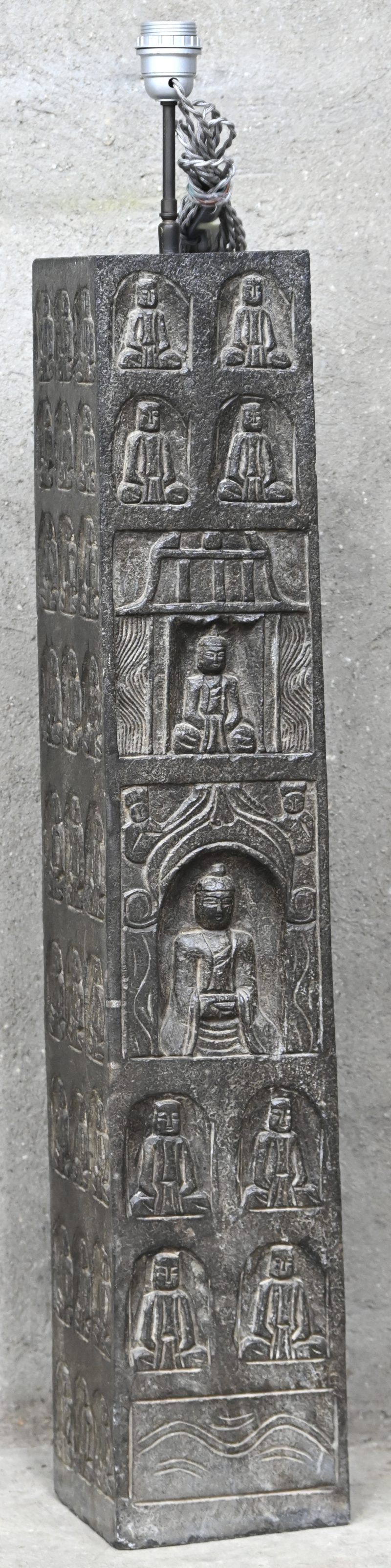 Een kamerlamp, gemonteerd op een vierhoekige natuurstenen zuil met een decor van zittende Buddha’s in kleine nissen.