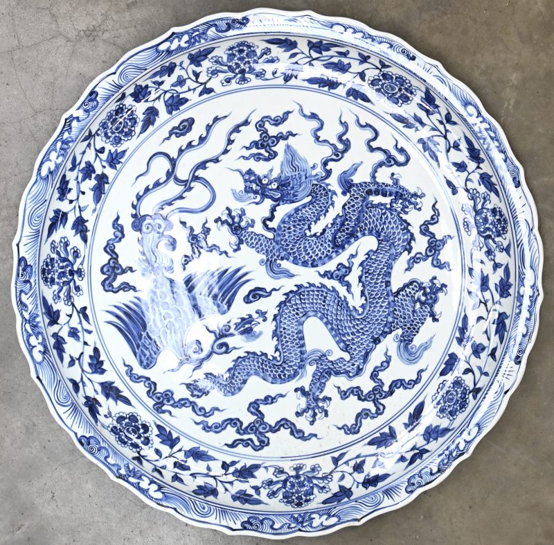Een groot formaat Chinees porseleinen schotel. Blauw-wit met draak en floraal decor.