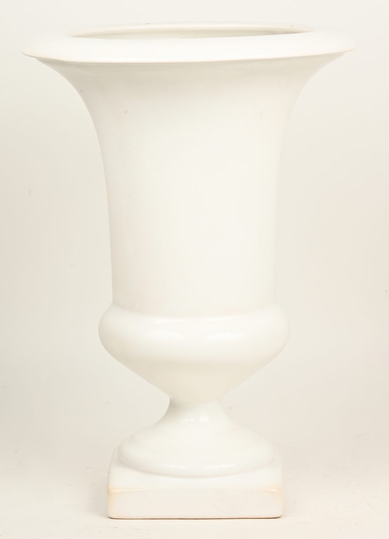 Een wit aardewerken vaas op voetstuk.