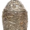 Een ronde theedoos van brons met een vegetaal reliëfdecor met op het deksel drie gezichten. Klein letsel aan de bovenrand.