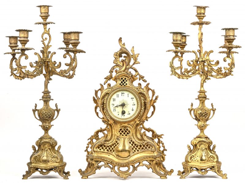 Een koperen klokstel in Lodewijk XV-stijl. Twee kandelaars met vijf lichtpunten. Met slinger en sleutel.