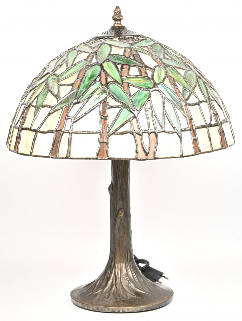 Een lamp in Tiffany-stijl met bronskleurige voet en glas in lood kap met bladeren in het decor.