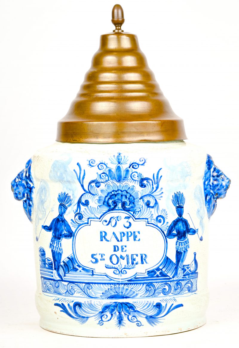 Een Delfts porseleinen tabakspot blauw-wit met opschrift en rokende Indiaan in het decor. Leeuwenhoofden aan de zijkant en onderaan gemerkt “De Porceleyne Clauw”.