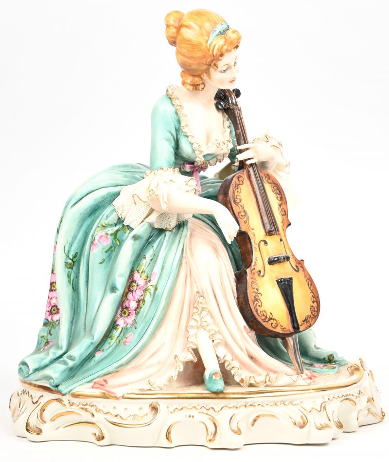 “De Cellospeelster”. Een meerkleurig porseleinen beeldje. Gelabeld Sonia by Cortese voor Capodimonte, onderaan gesigneerd.