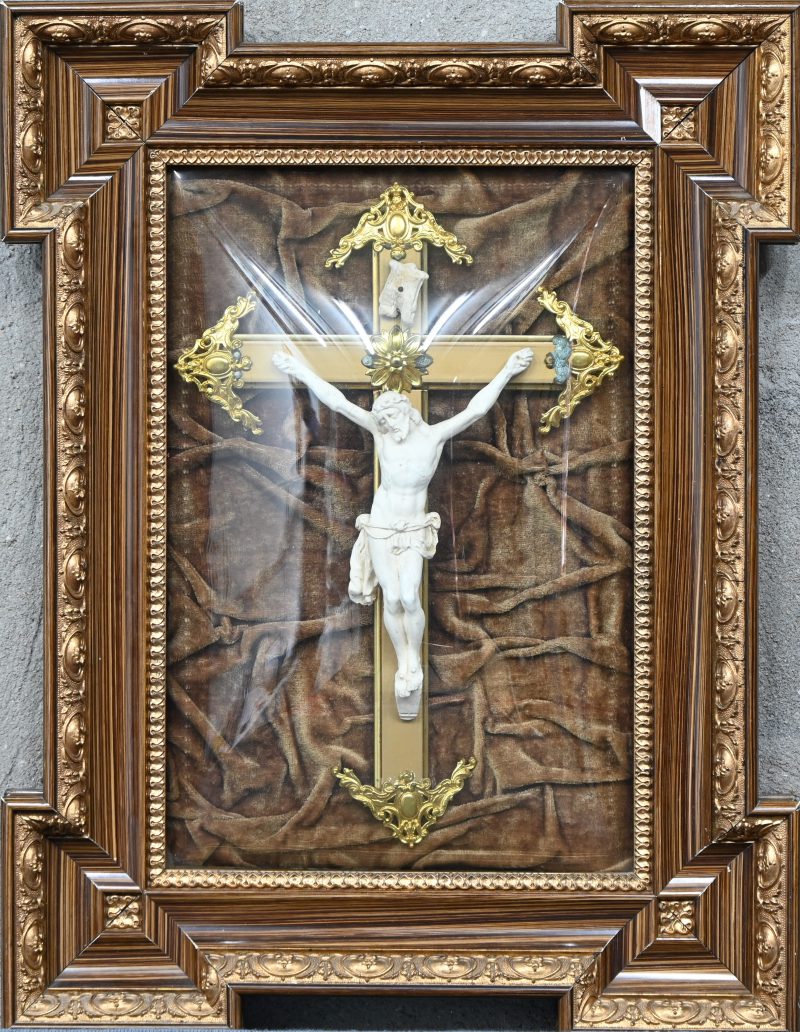 Een kruisbeeld in biscuit in een kader met bol glas.
