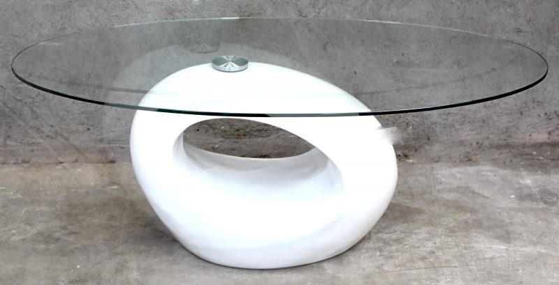 Een salontafel met organisch gevormde kunststoffen basis in witte hoogglans en ovaalvormig glazen blad.