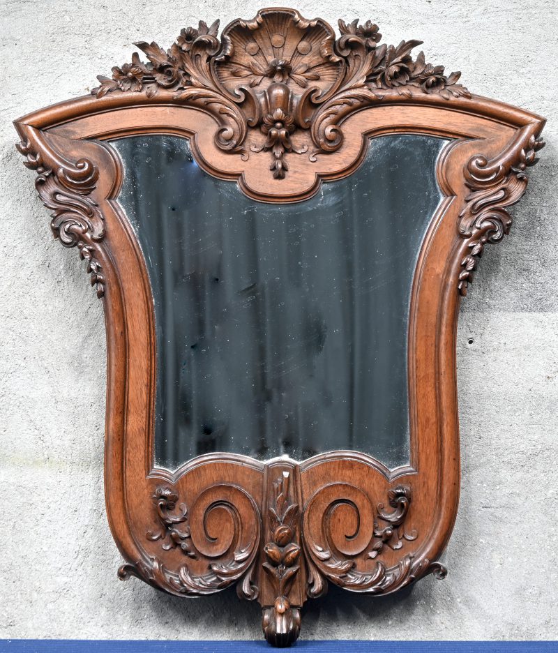 Een spiegel in gebeeldhouwde kader in notelaar met weelderige kuif.