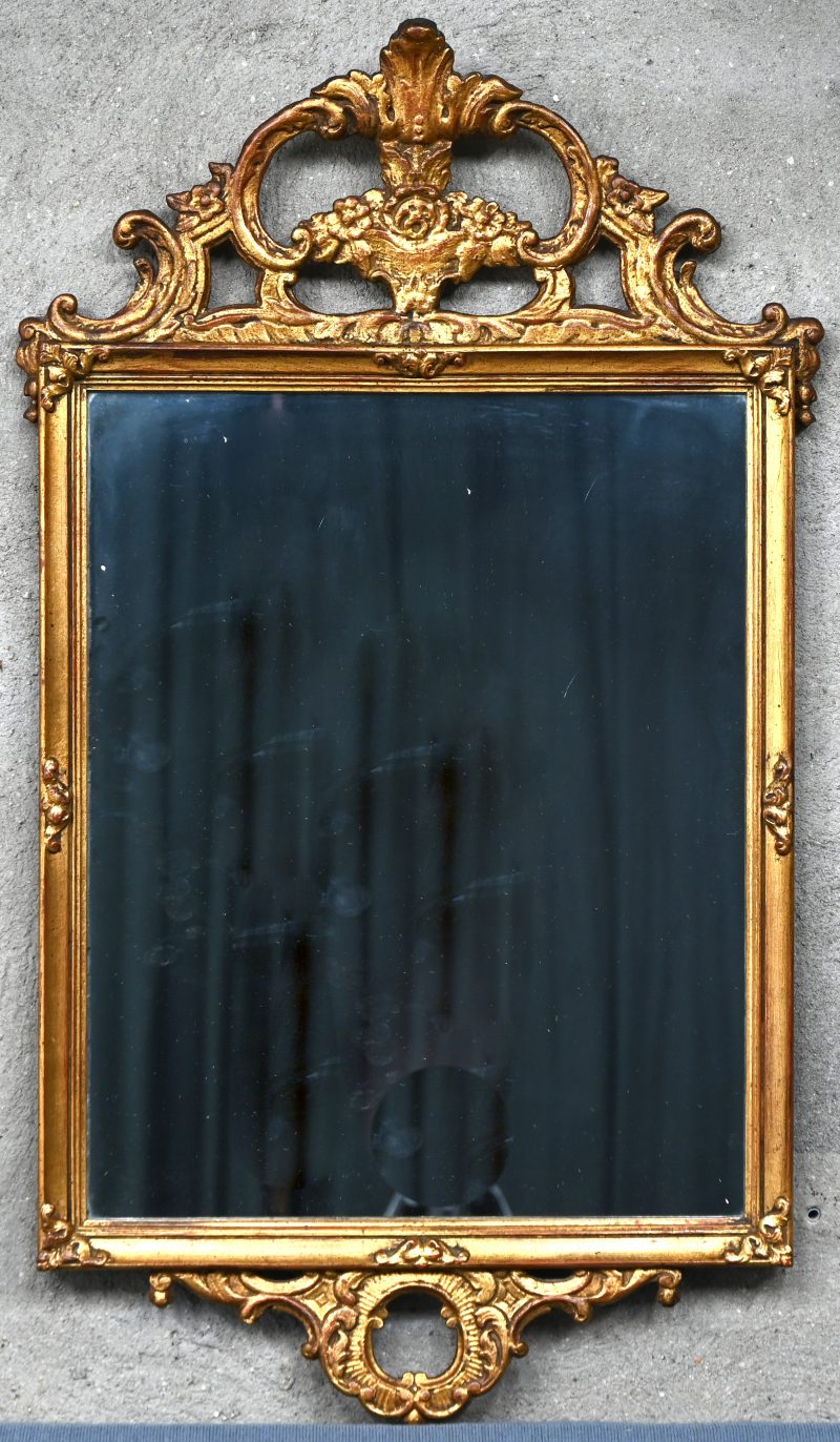Een spiegel in polychroom verguld houten kader met gesculpteerde elementen.