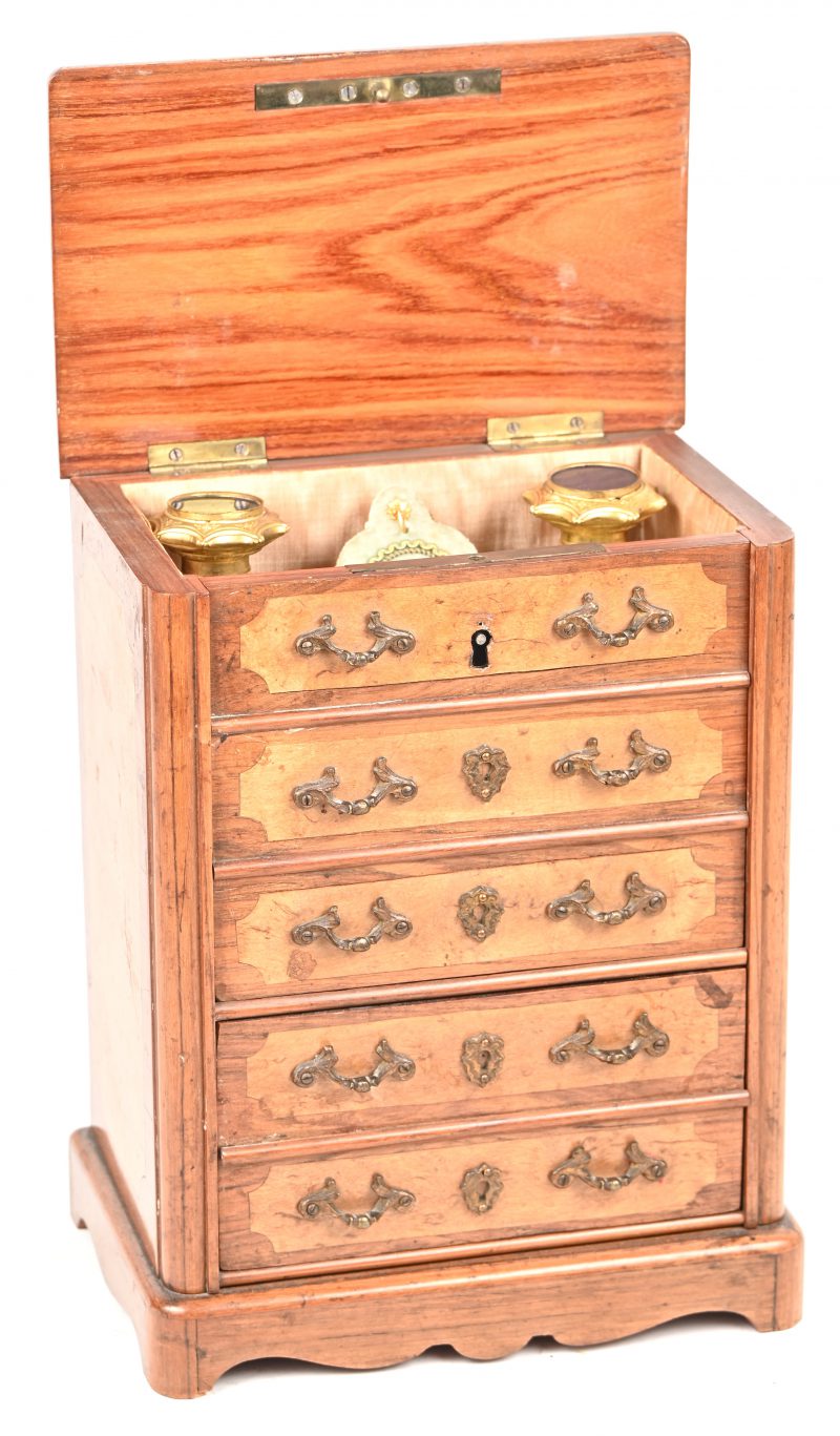 Een 19e eeuws juwelenkistje met bijhorende parfumflesjes met vergulde dopjes in de vorm van een ladekastje in oa. notenfineer. Er ontbreekt één trekkertje aan het verborgen laatje. Het plaatje voor het sleutelgat is nog aanwezig.