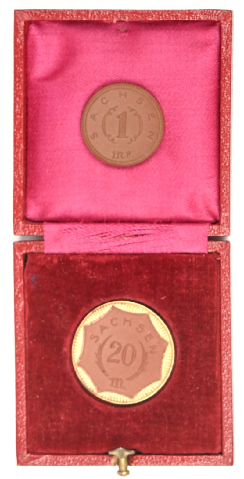 Een lotje van twee Sachsen munten in rood porselein, 1 Mark en 20 Mark, de laatste met vergulde rand. In foedraal.