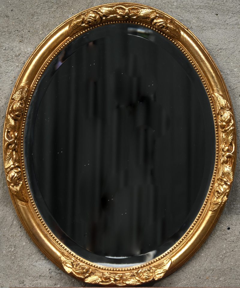 Een ovalen spiegel in geslepen glas met verguld houten kader en florale ornamenten.