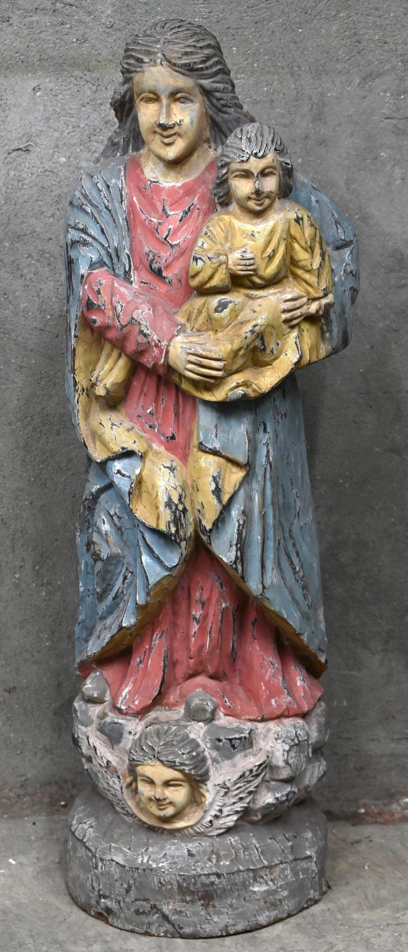 Een groot polychroom houtgesculpteerd beeld van de heilige moeder met haar zoon op de arm. Het beeld heeft een grote barst.