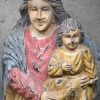 Een groot polychroom houtgesculpteerd beeld van de heilige moeder met haar zoon op de arm. Het beeld heeft een grote barst.