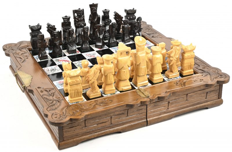 Een opvouwbaar Oosters schaakbord in gesculpteerd hout. De schaakstukken zitten in twee laden in het bord.