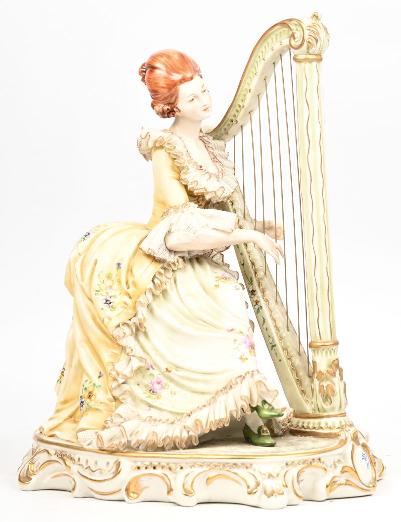 “De Harpspeelster”. Een meerkleurig porseleinen beeldje. Mist één vinger.