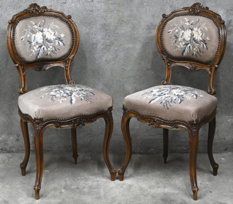 Een paar eikenhouten Louis XV stijl stoelen met gesculpteerde details, gobelin zitting en geborduurd floraal decor.