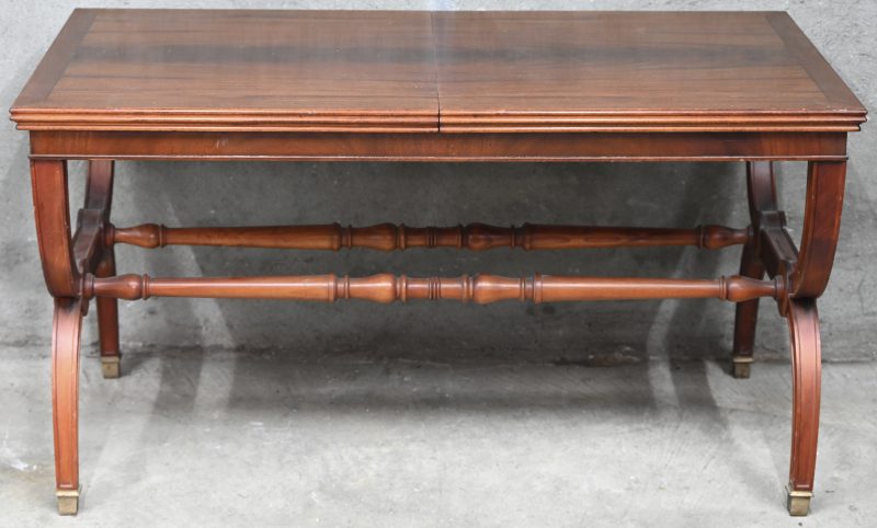 Een antiek houten salontafel met gebogen X vorm poten en uitschuifbaar blad met glazen midden.