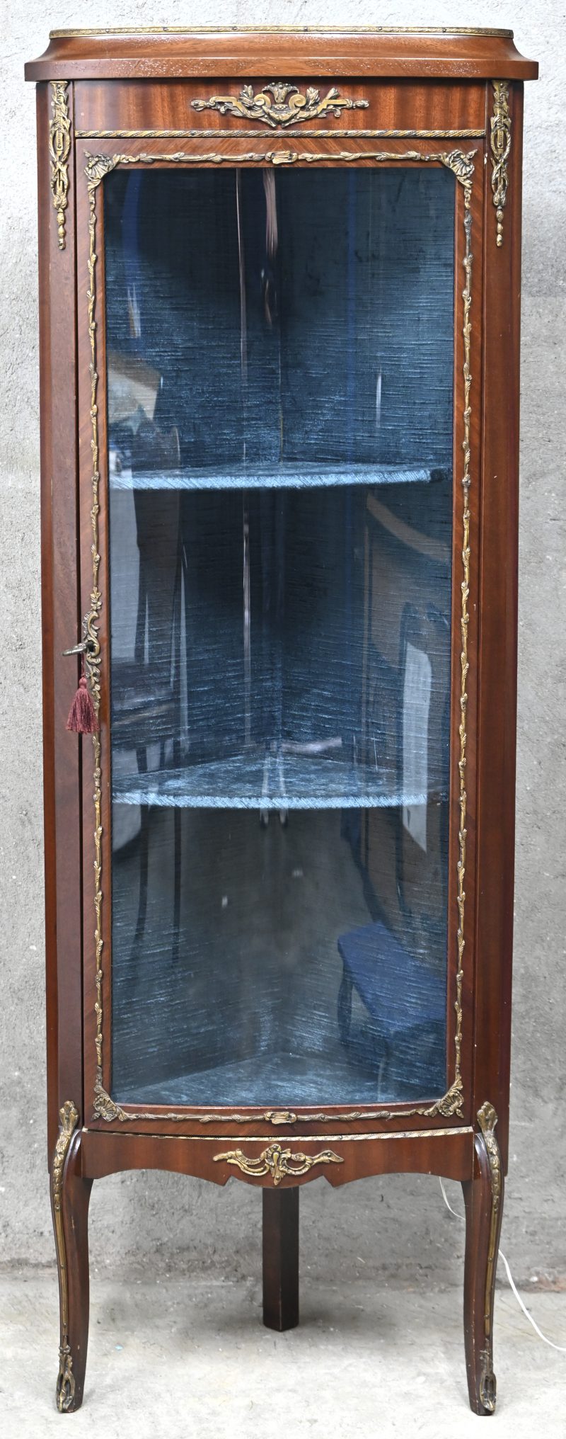 Een houten hoekvitrine met gebogen glazen deur, 2 schabben en messingen monturen.