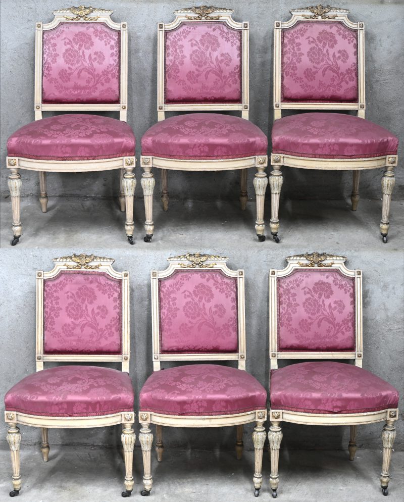 Een set van zes Franse houtgesculpteerde stoelen, ecru en goudkleurig gepatineerd met oud-roze stof met bloemmotieven bekleed. Wieltjes vooraan.