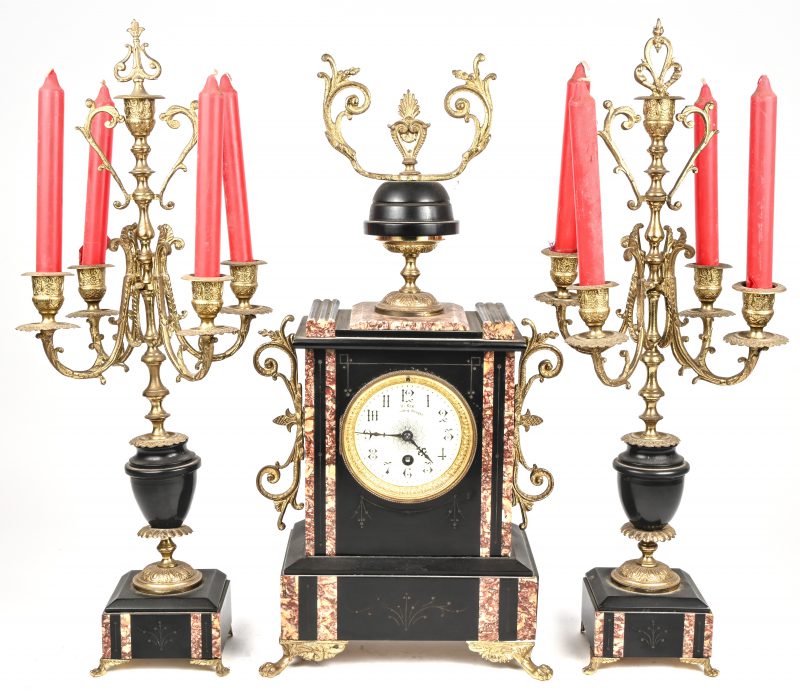 Een driedelig schouwgarnituur in marmer en koper bestaande uit een klok en twee kandelaars. De klok draagt het opschrift H. Six Bruges.