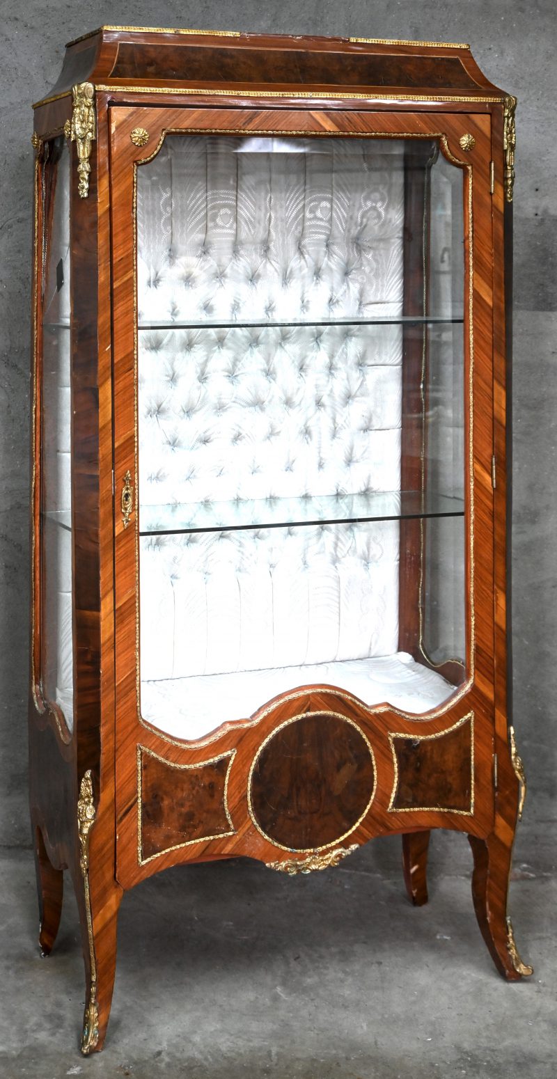 Een ééndeurs vitrinekast, Louis XVI geïnspireerd, gefineerd hout. Het glas aan de linkerzijde is gebarsten.