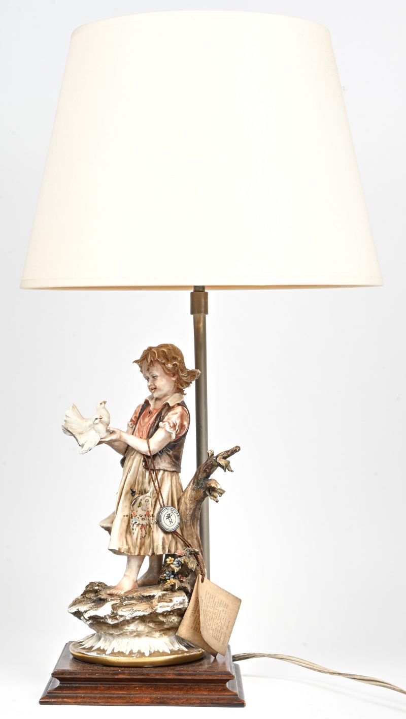 Een vintage porseleinen tafellamp met beeld van een meisje met 2 duiven en gestoffeerde kap. Gemerkt en gelabeld Capodimonte. Onderaan gesigneerd.