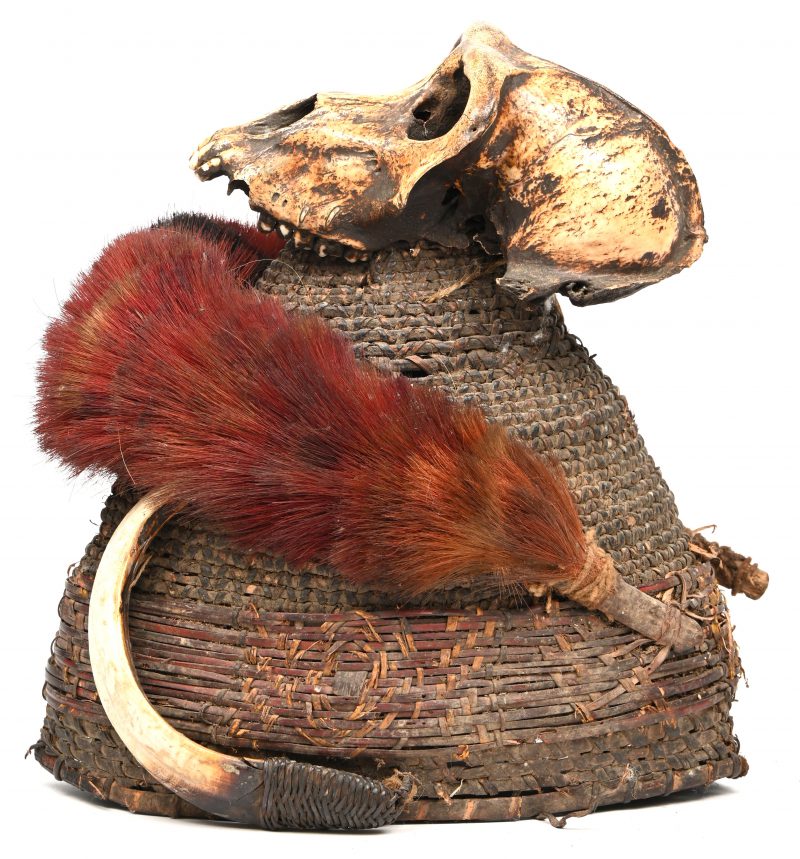 Een ceremoniële hoed van de Naga, vervaardigd uit gewoven bamboe, versierd met een apenschedel en zwijn slagtanden. Nagaland, Indië, vroeg 20e eeuw.