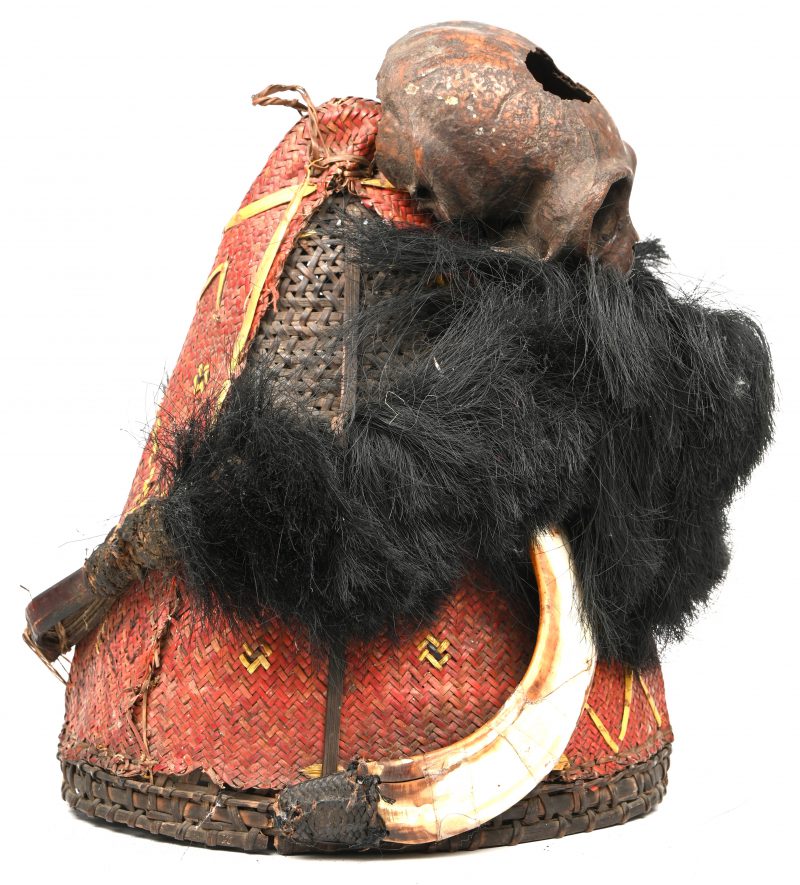 Een ceremoniële hoed van de Naga, vervaardigd uit gewoven bamboe, versierd met een apenschedel en zwijn slagtanden. Nagaland, Indië, vroeg 20e eeuw.