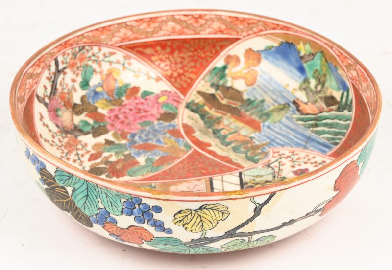 Een ronde coupe met hoge rand van veelkleurig Japans porselein versierd met diverse voorstellingen in uitsparingen. Oude restauraties en beschadigingen. Gemerkt Kutani.