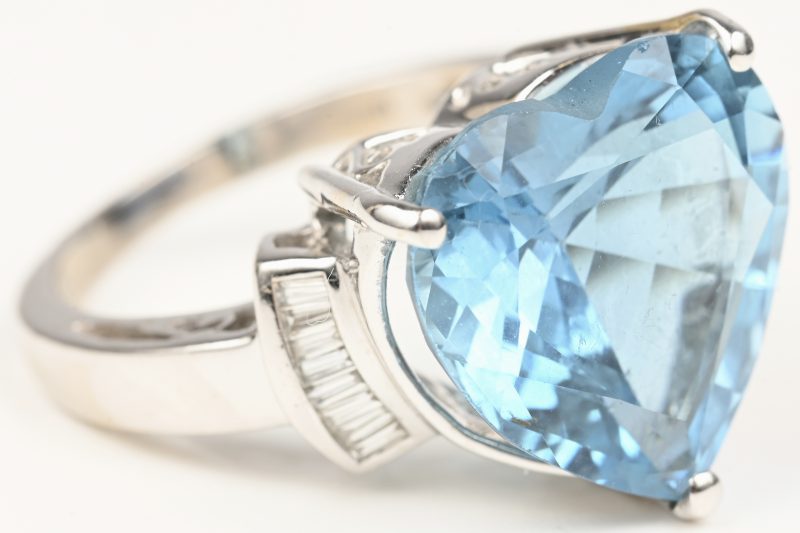 Een 18 kt witgouden ring bezet met een hartvormige blauwe topaas van +- 11,07 ct. en diamand baguetten met een gezamenlijk gewicht van +- 0,24 ct. Mer certificaat.