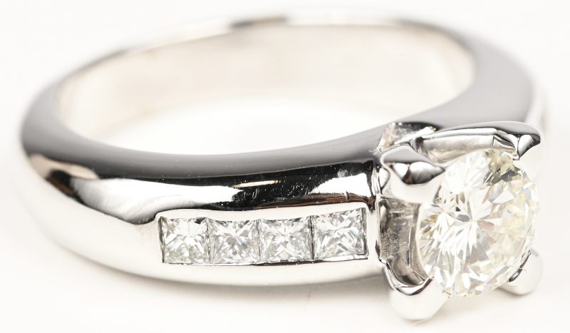 Een 18 kt witgouden ring bezet met een centrale briljant van 0,93 ct. GSI1 en diamanten princes cut met een gezamenlijk gewicht van +- 0,60 ct.