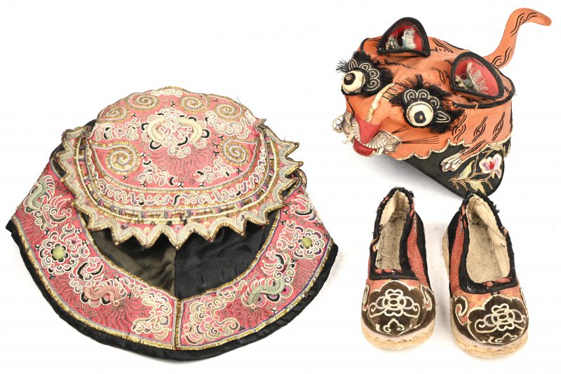 Een lot Chinees traditionele klederdracht, bestaande uit een paar Manchu geborduurde schoentjes en 2 kinderhoedjes met diverse versiering.
