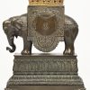 Een bronzen olifant op sokkel, als speldenkussen met een verborgen mechanisme dat een verguld bronzen kindje Jesus verbergt. Opschriften “Stat semper linea recta” en “Tant que vive”, respectievelijk de wapenspreuken van de families de Ligne en de Trazegnies. Mooi voetstuk versierd met acanthusfriezen. XIXde eeuw.