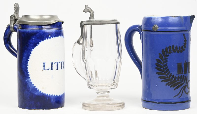 Een lot van 3 bierpullen waarvan 2 in blauw en wit aardewerk met opschrift ‘LITRE’, beide gemerkt waarvan op de ene W21, de andere niet meer leesbaar. En een kristallen pul. Eén pul ontbreekt het tinnen deksel en vertoont schilferschade alsook haarlijnscheurtjes en een restauratie.