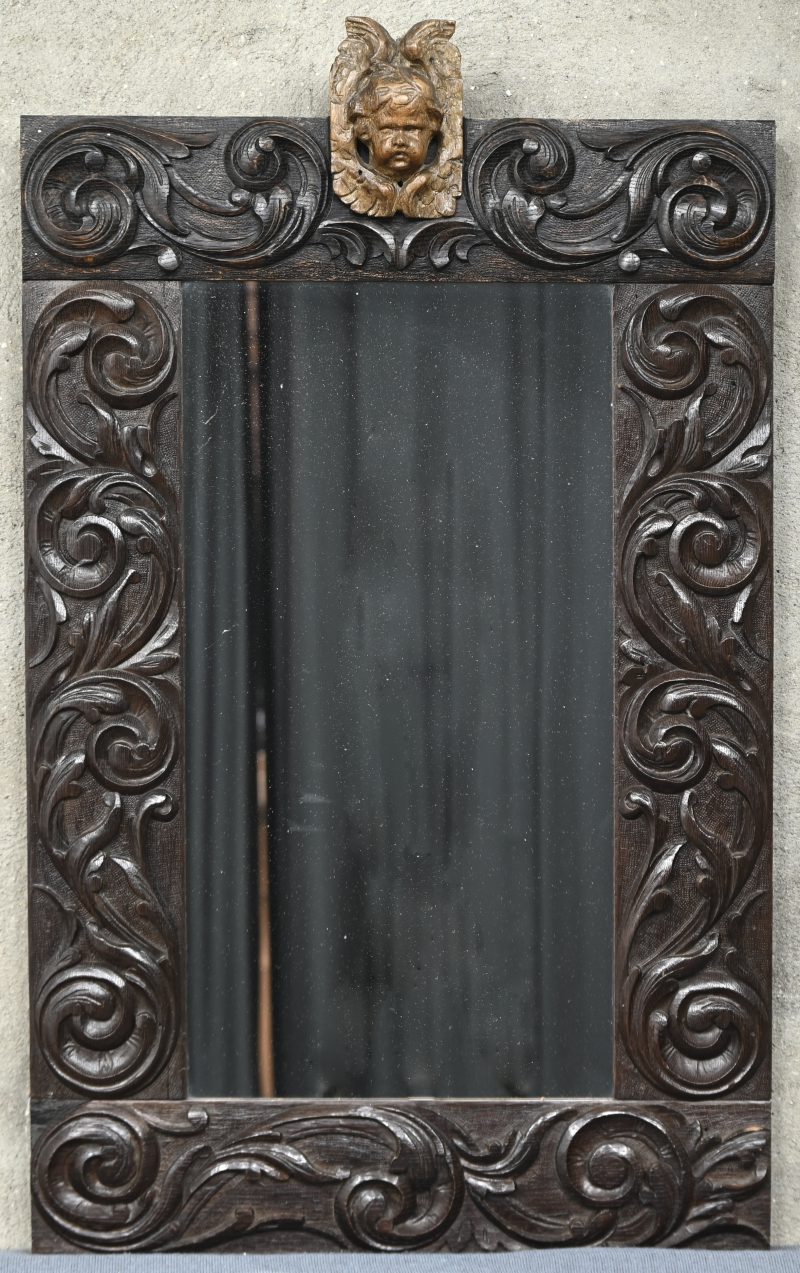 Een spiegel in massief houten gesculpteerde kader en bovenaan een engelenhoofdje gemonteerd.