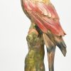 Een vintage polychroom keramisch beeld van een papegaai op een boomstronk.