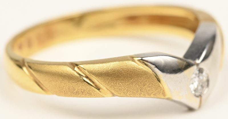Een 18 kt wit en geelgouden ring bezet met één briljant van +- 0,10 ct.