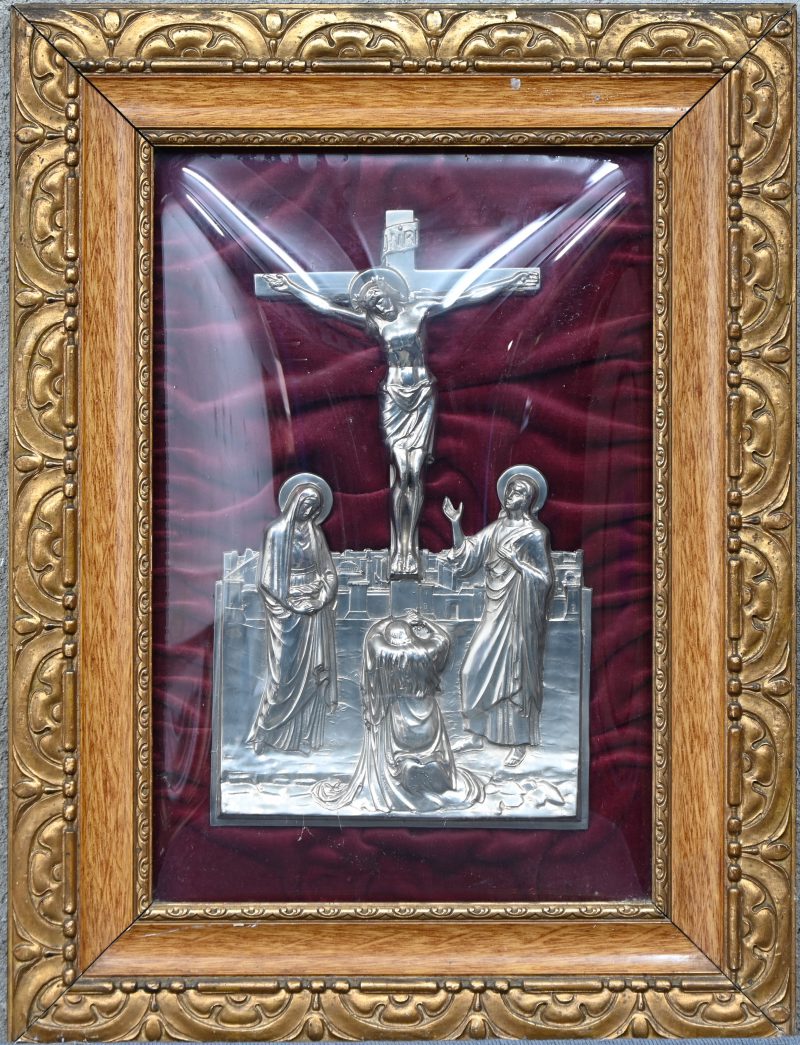 Een verzilverde religieuze voorstelling van Jezus aan het kruis in een kader met bol glas.