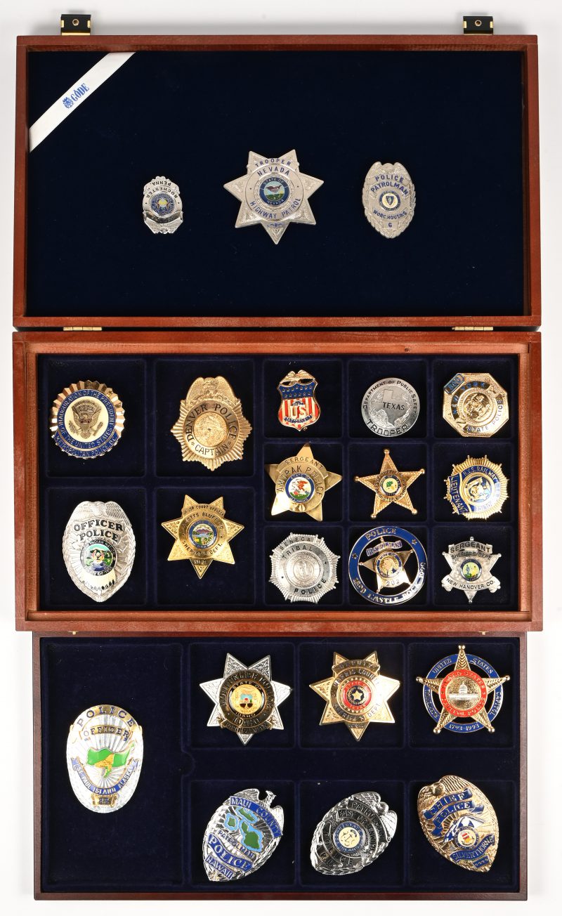 Een lot van 23 State-Police insignes uitgebracht door Gode. In een verzamelkoffertje.
