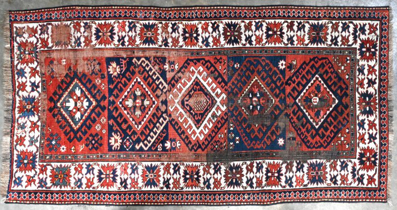 Een oud handgeknoopt oosters tapijt met meerdere slijtagevlekken.