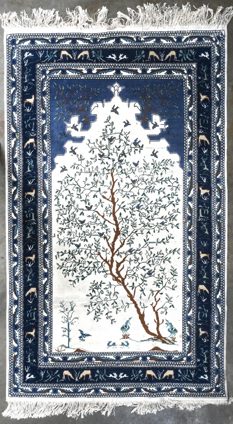 Een handgeknoopt oosters tapijt, blauw en wit met dieren en een boom.
